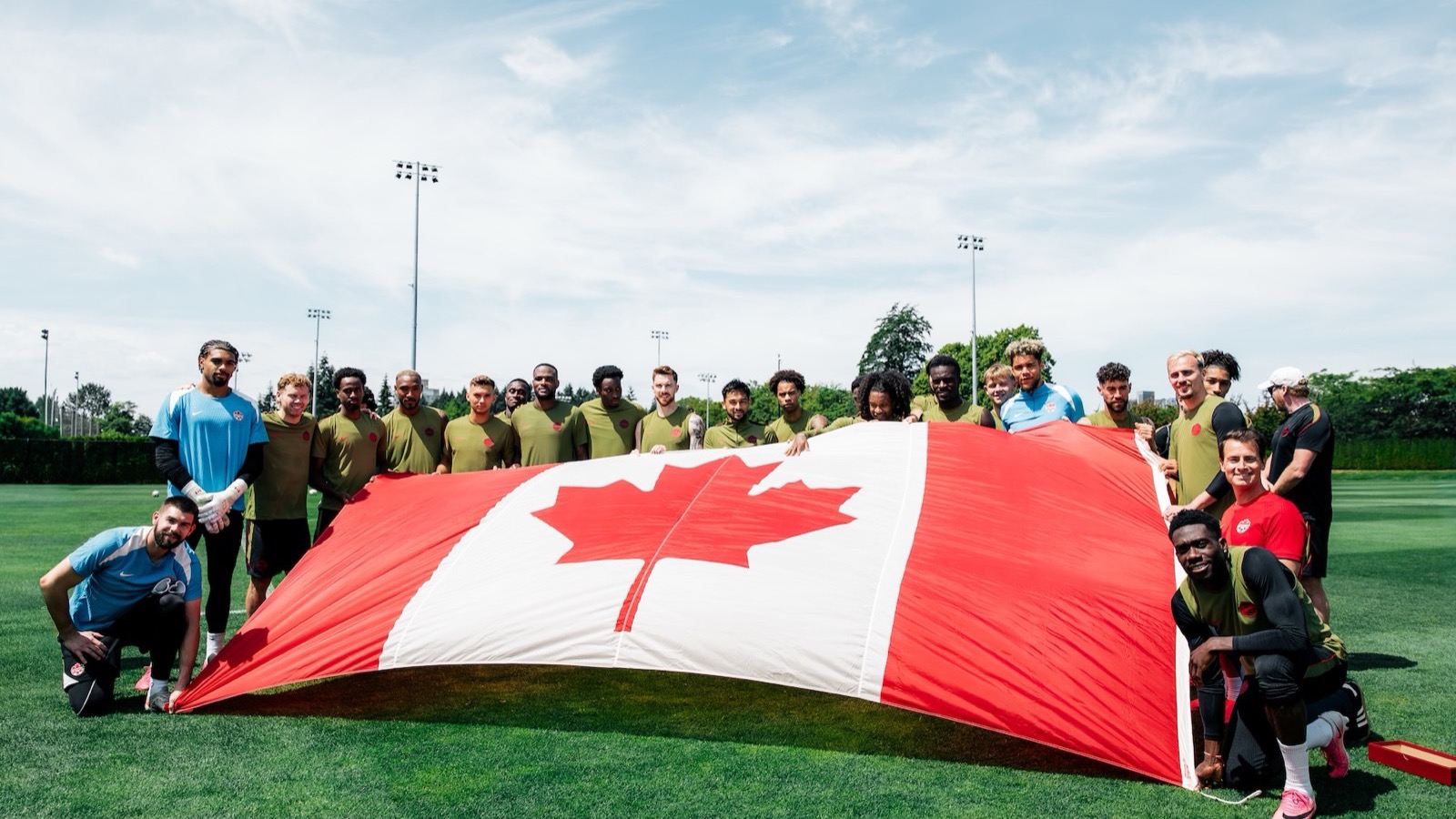 Canada men's national team players pose with a large national flag at training